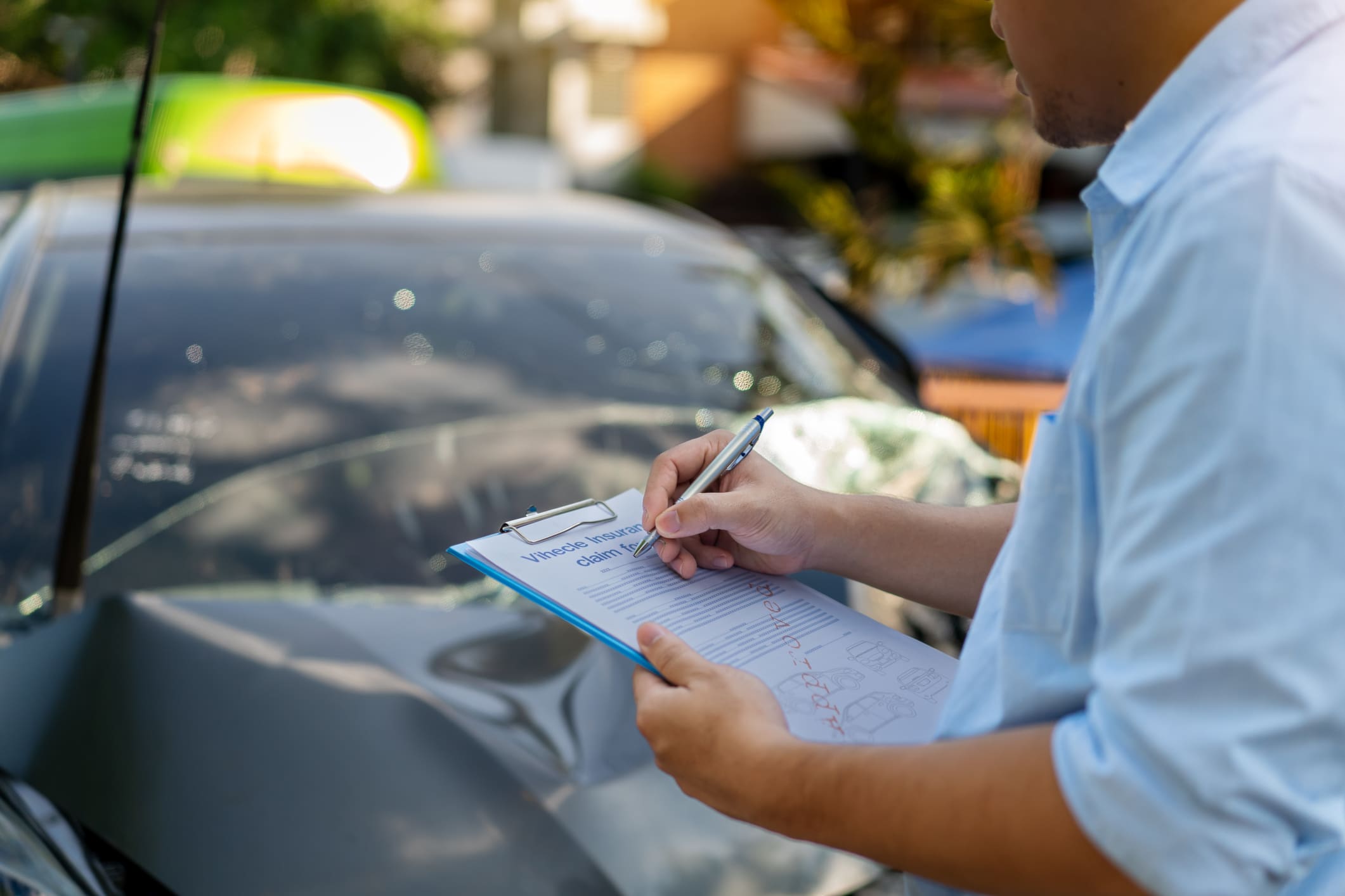 Person writing a parking ticket on a clipboard beside a car.